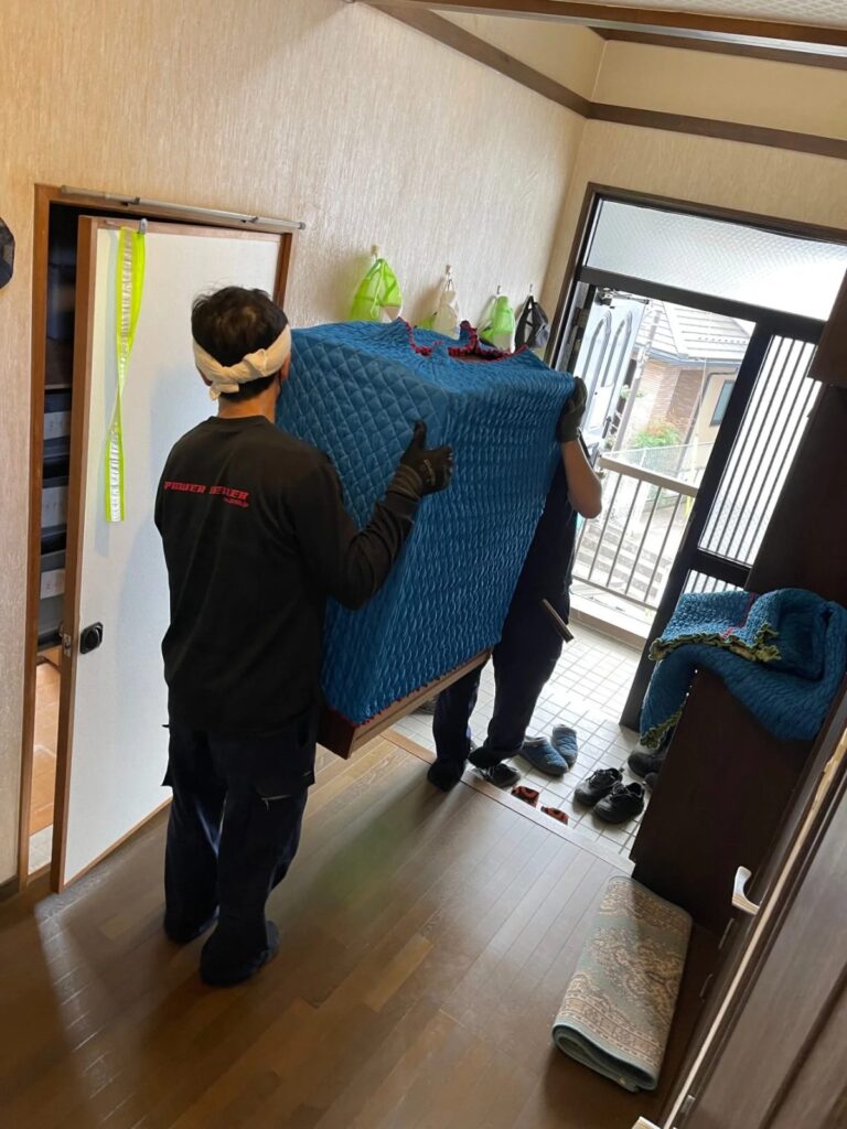 養生した大型家具を2名のスタッフが玄関先へ搬出している作業
