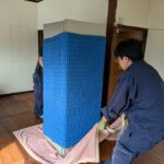 養生材で包んだ6ドア冷蔵庫を毛布に載せて室内を移動する作業スタッフ