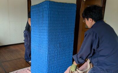 養生材で包んだ6ドア冷蔵庫を毛布に載せて室内を移動する作業スタッフ
