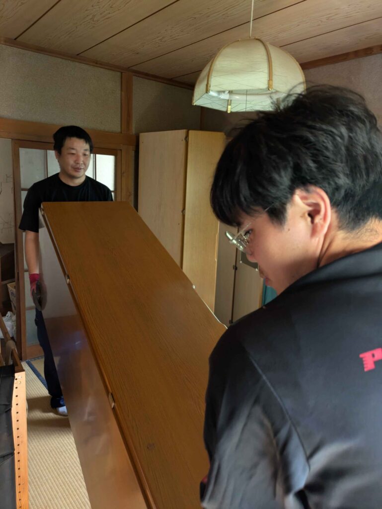 和室から大型の収納家具を2人で運び出す様子