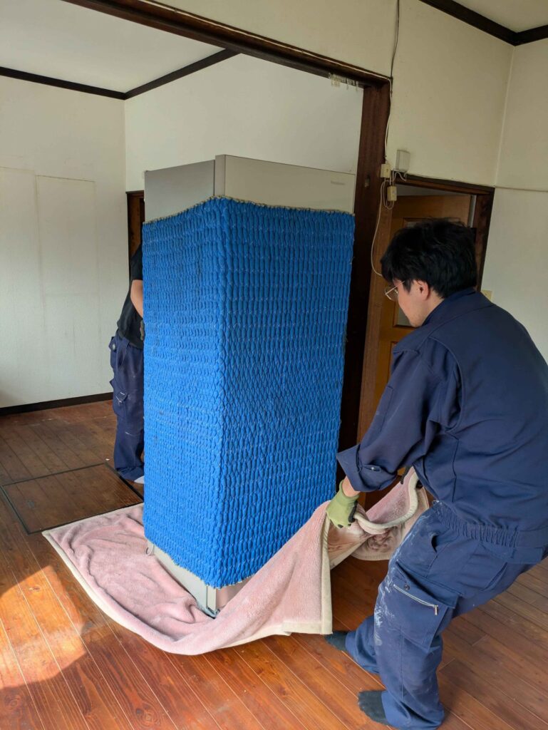 保護カバーを掛けた冷蔵庫を毛布の上で移動する様子