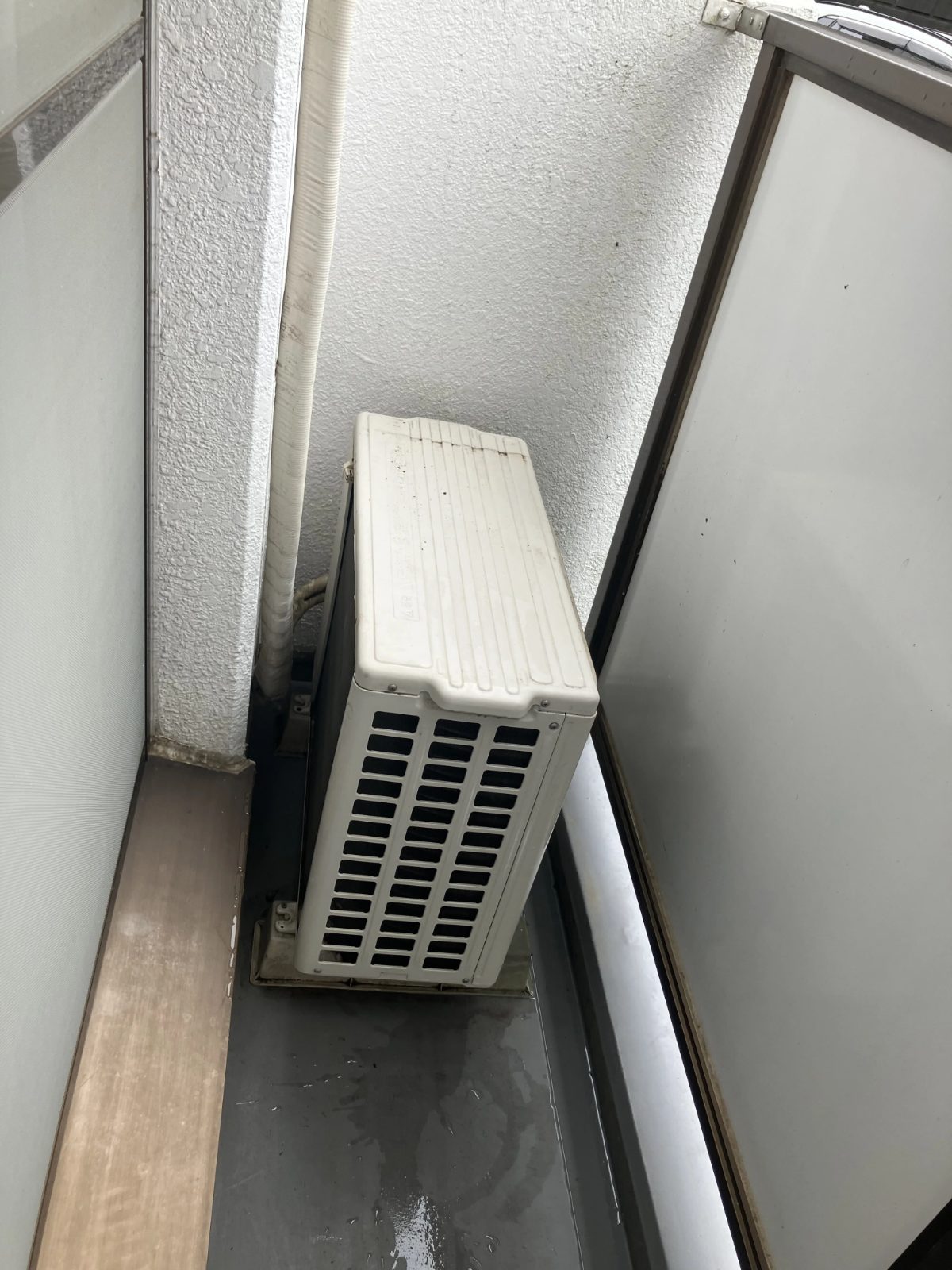 ベランダに床置きされたエアコン室外機の写真（取り外し前の確認用）