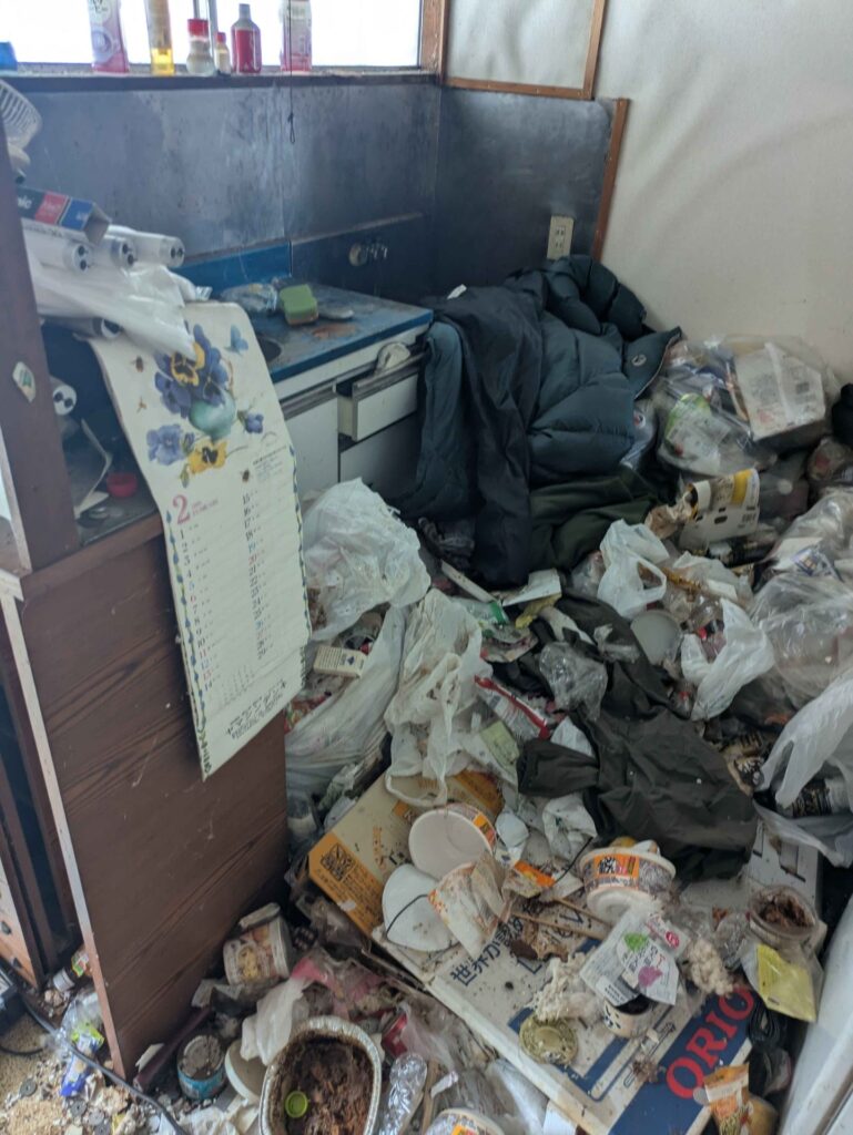 作業前の台所。床一面に生活ごみと衣類が積み重なった状態