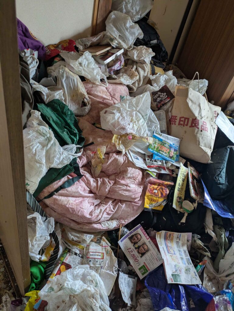 作業前の和室。布団や衣類、チラシが積み重なっている