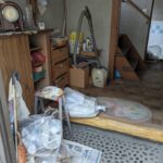 作業前の玄関。上がり口に袋に入った日用品や掃除機、棚が残っている