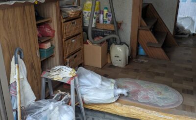 作業前の玄関。上がり口に袋に入った日用品や掃除機、棚が残っている