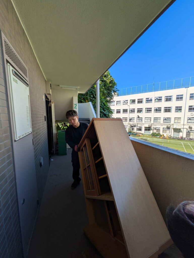 マンションの外廊下で大型の木製キャビネットを運び出す当社スタッフ
