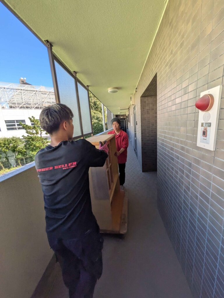 外廊下でガラス扉の食器棚を運ぶ当社スタッフの後ろ姿