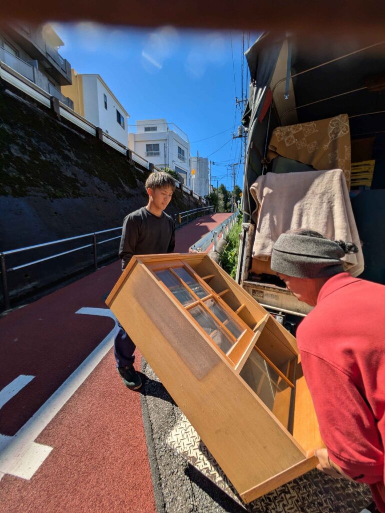 階段の下で食器棚の向きを変えてトラックへ運ぶ様子