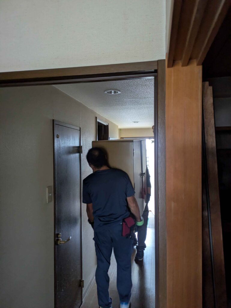 室内の廊下から大型の家具を運び出す当社スタッフ