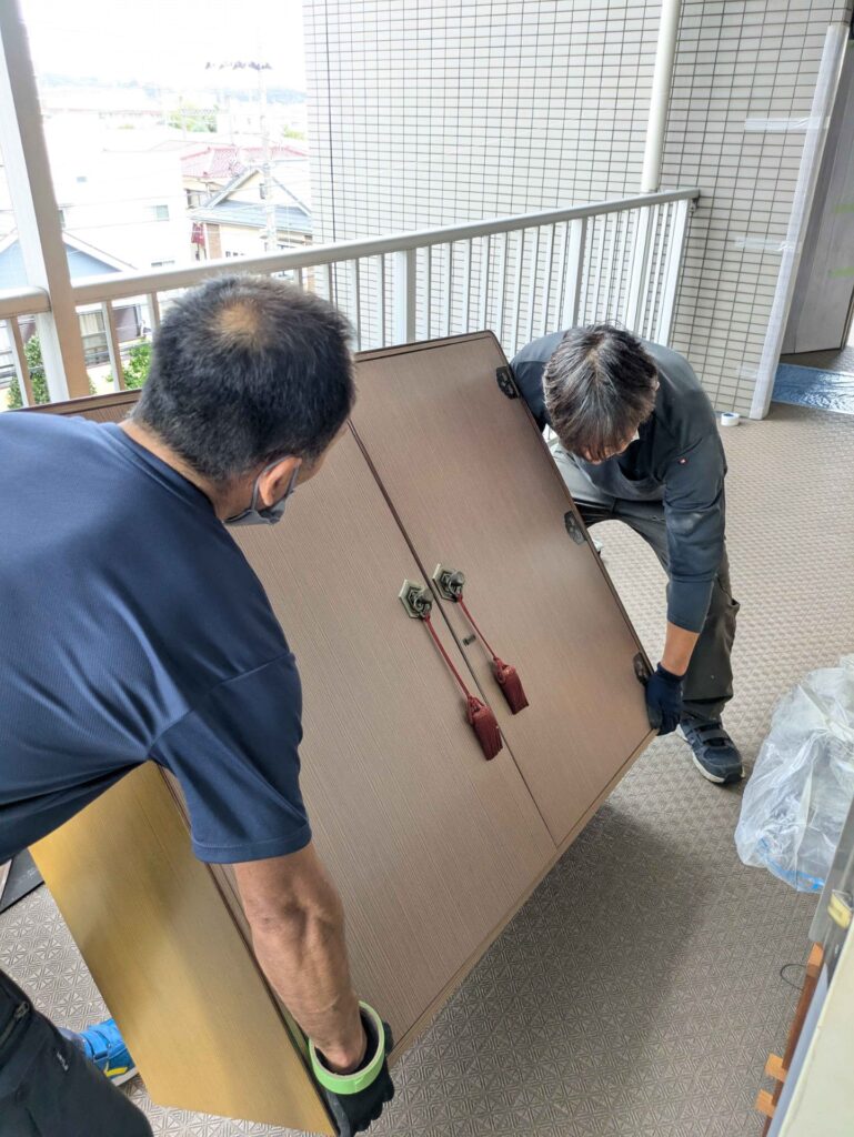 マンション4階の共用廊下で洋服ダンスを2人で運ぶ様子