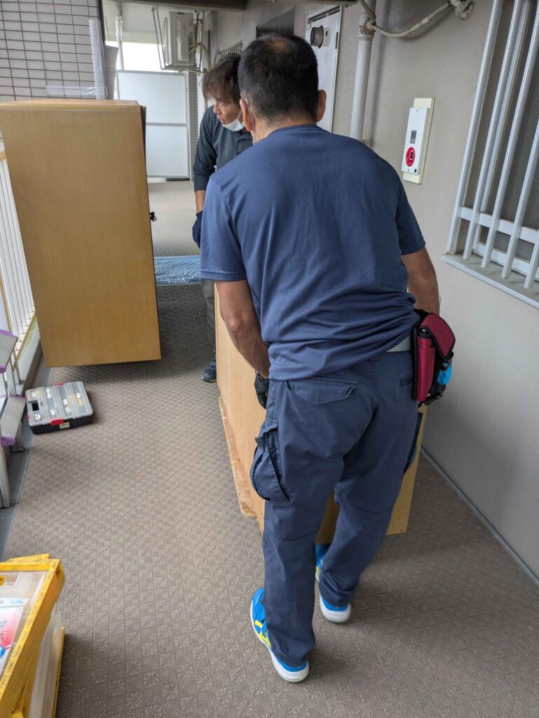 共用廊下で家具を台車に載せてエレベーターへ運ぶ当社スタッフ