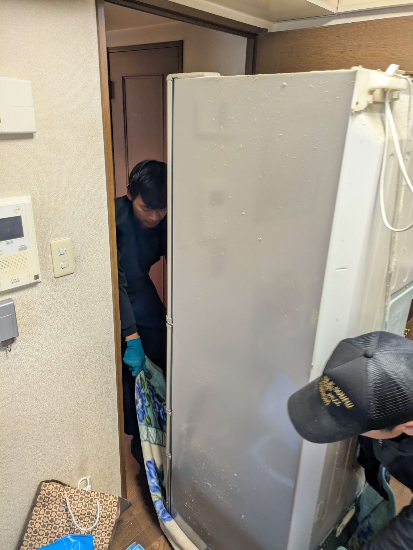 毛布をかけた冷蔵庫を2人で狭い廊下から運び出す