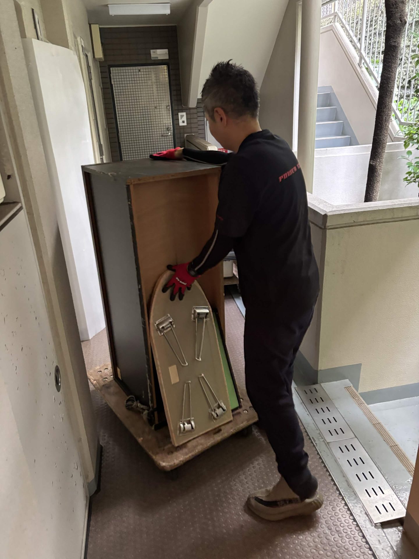 マンションの共用廊下で家具を台車に載せて運ぶ当社スタッフ